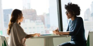 Dos mujeres conversan sentadas frente a una mesa