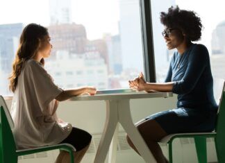 Cómo decir que no en el trabajo con asertividad: frases prácticas Dos mujeres conversan sentadas frente a una mesa